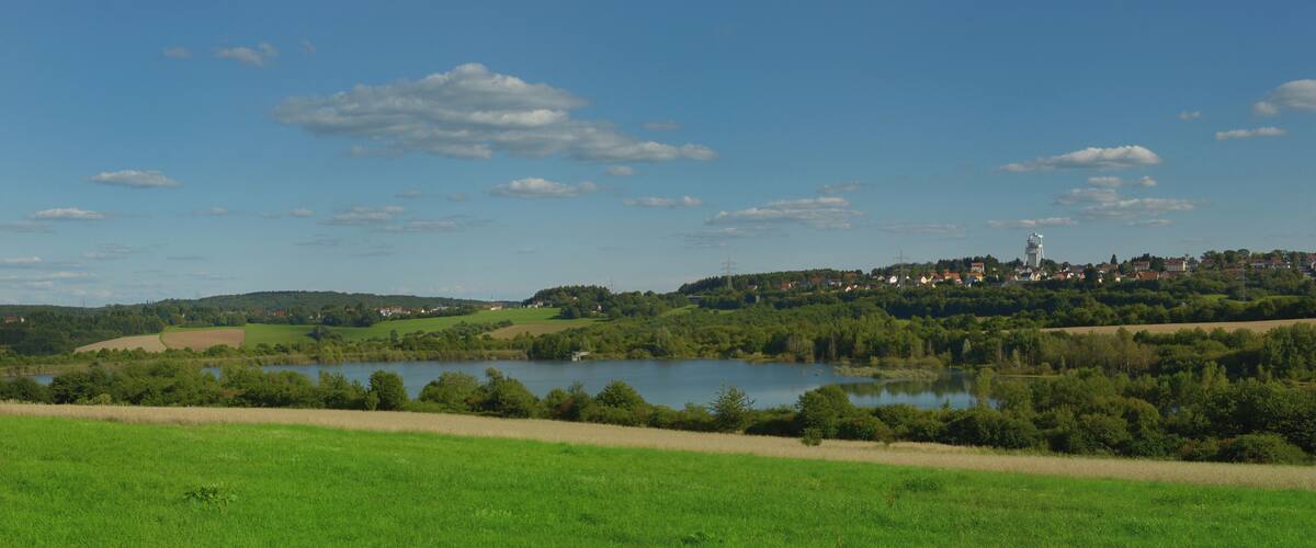A lake surrounded by green fields and a town with a water tower on a hill.