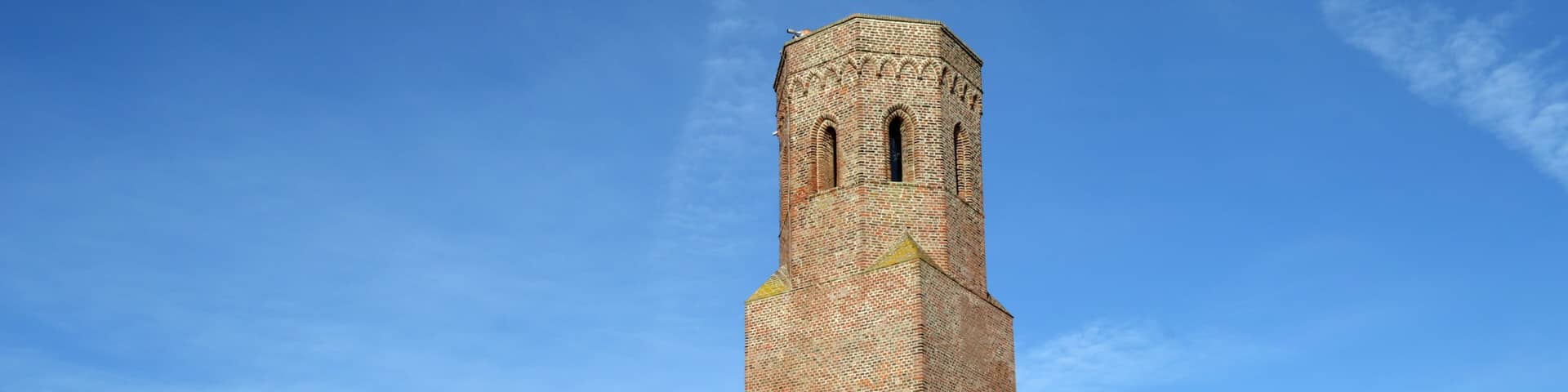 A tall brick tower with a pointed roof, surrounded by a grassy field and a clear blue sky.