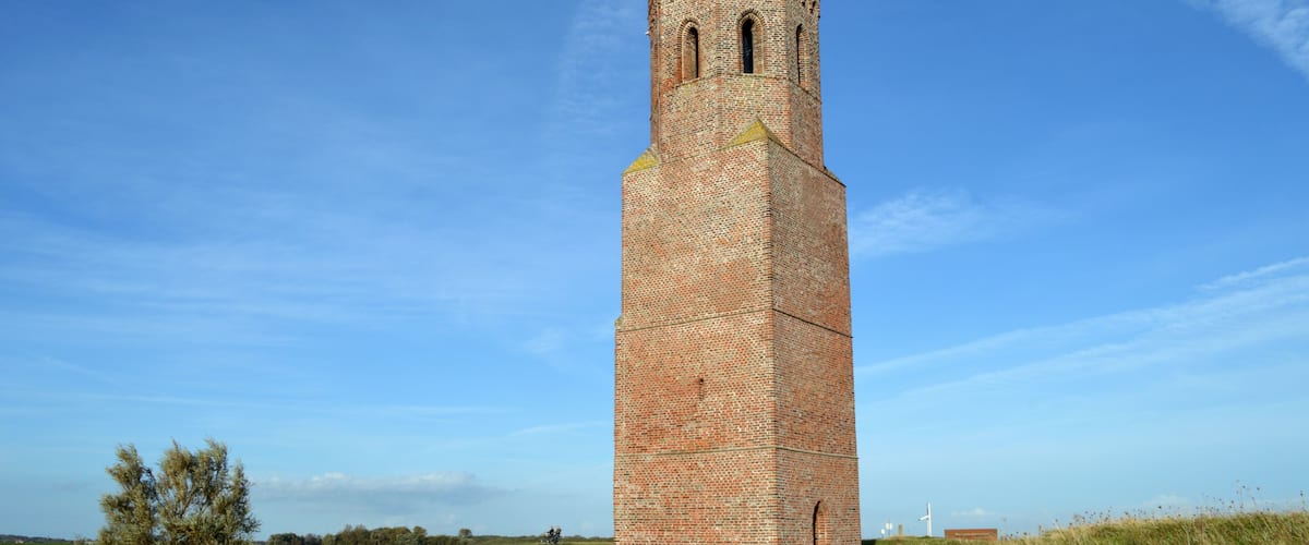 A tall brick tower with a pointed roof, surrounded by a grassy field and a clear blue sky.