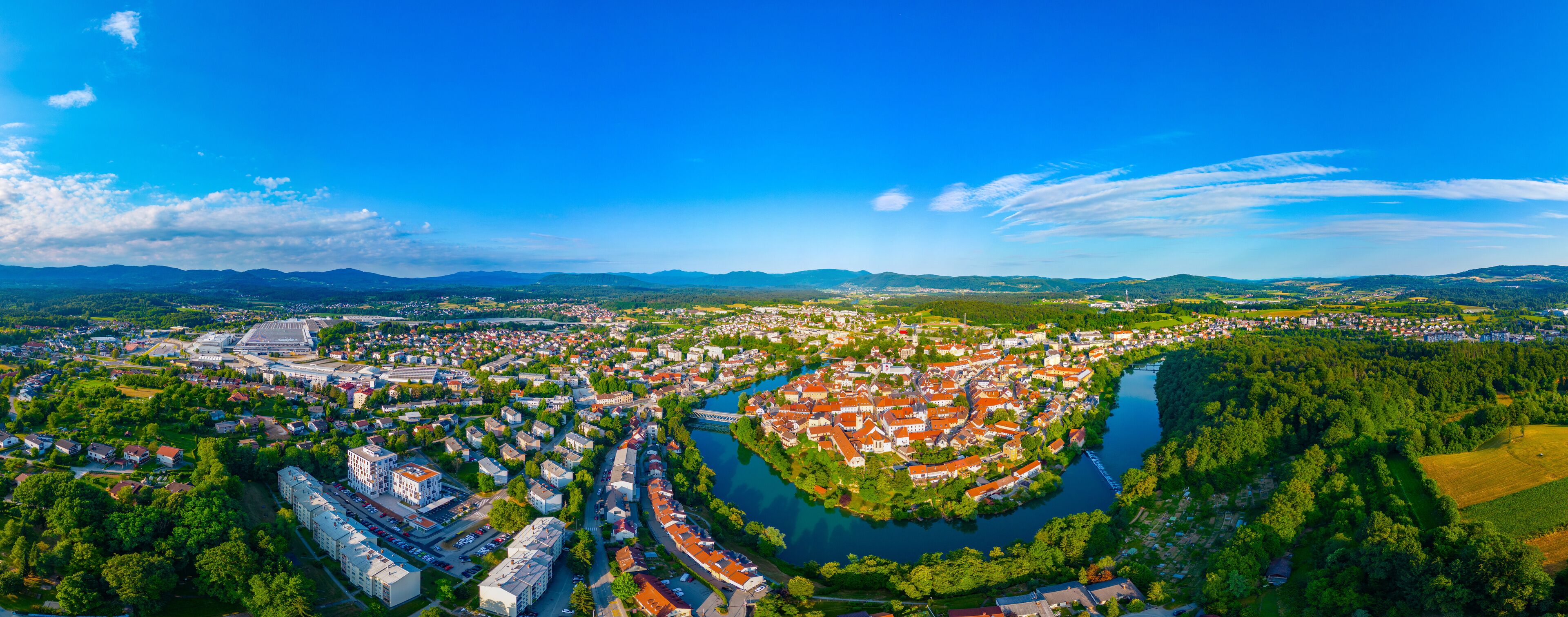 An aerial view of a town with a river, surrounded by mountains and greenery.