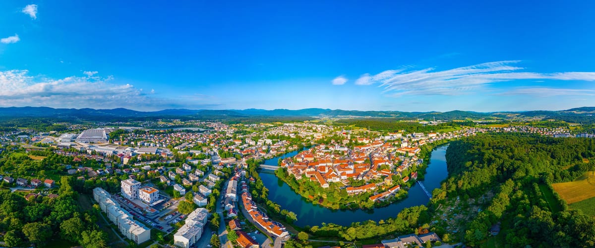An aerial view of a town with a river, surrounded by mountains and greenery.