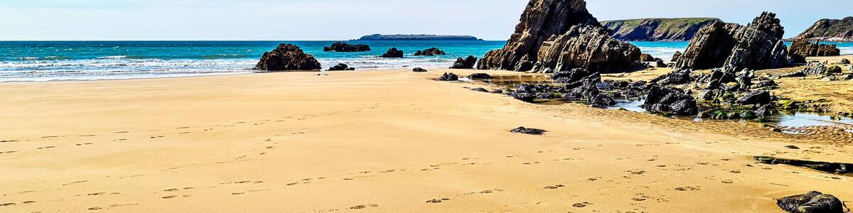 Ein sandiger Strand mit Felsformationen und einem klaren, blauen Himmel.
