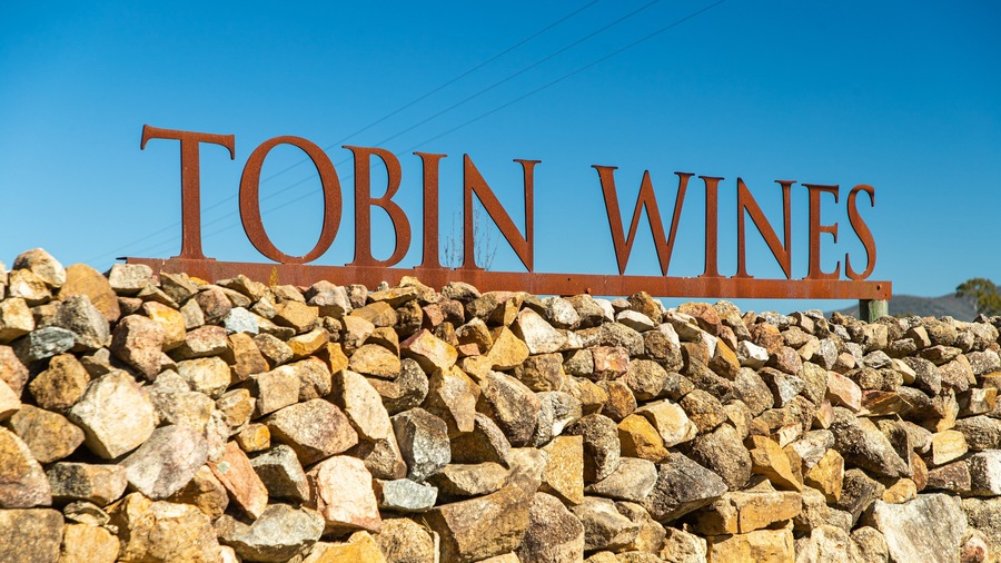 A sign for Tobin Wines with a stone wall in the foreground.