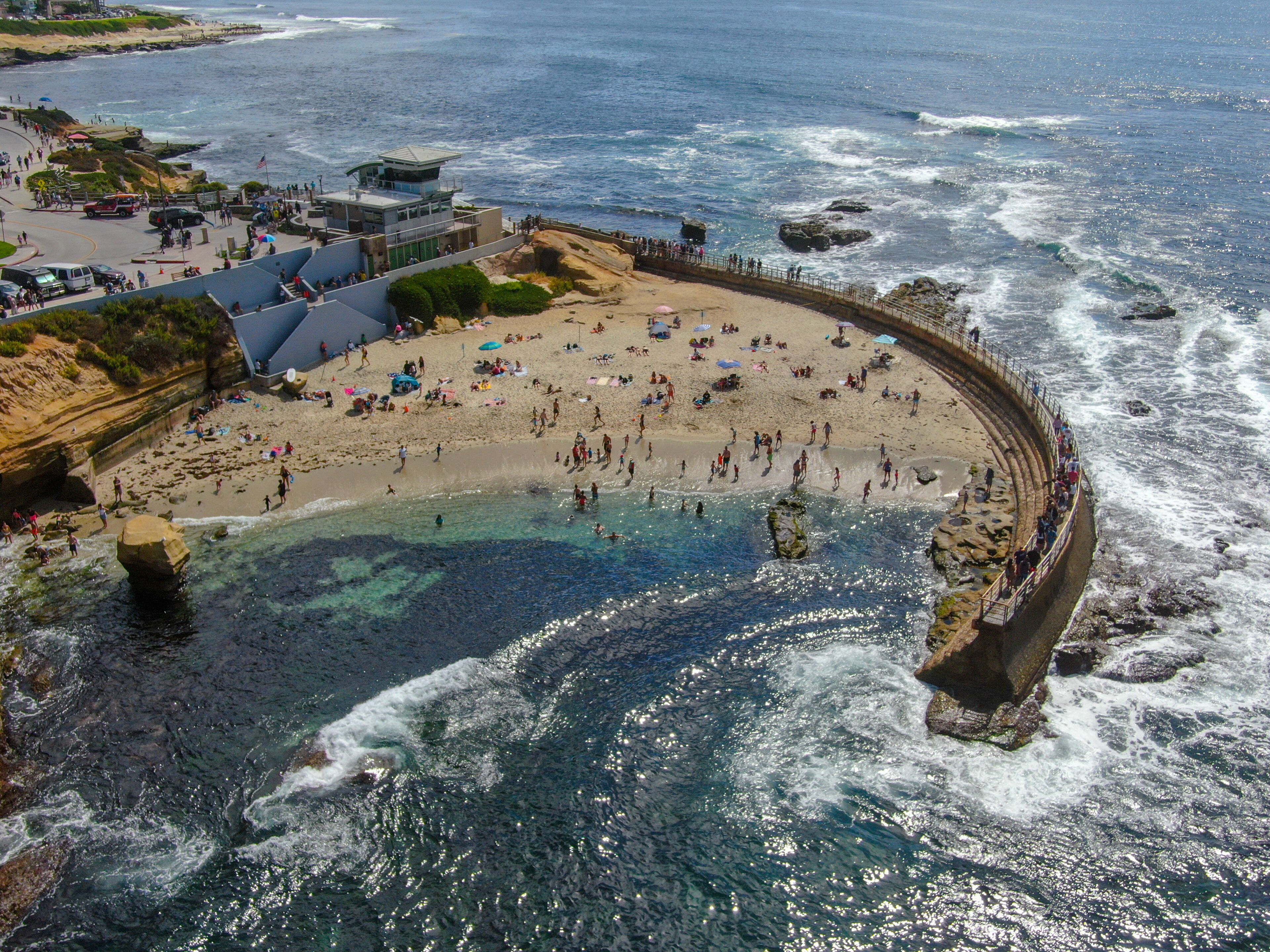 Una playa costera con aguas cristalinas, formaciones rocosas y un paseo curvo a lo largo de la orilla.