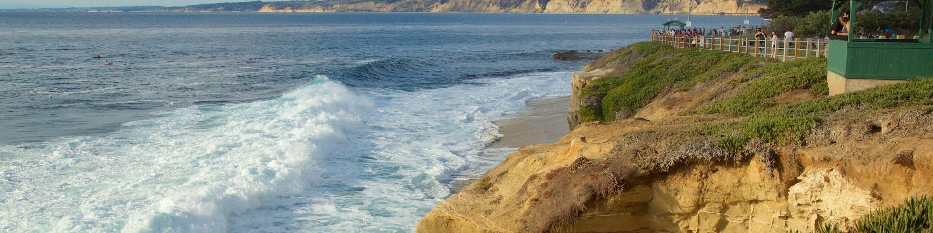 A coastal landscape with cliffs, waves, and a green structure overlooking the beach.