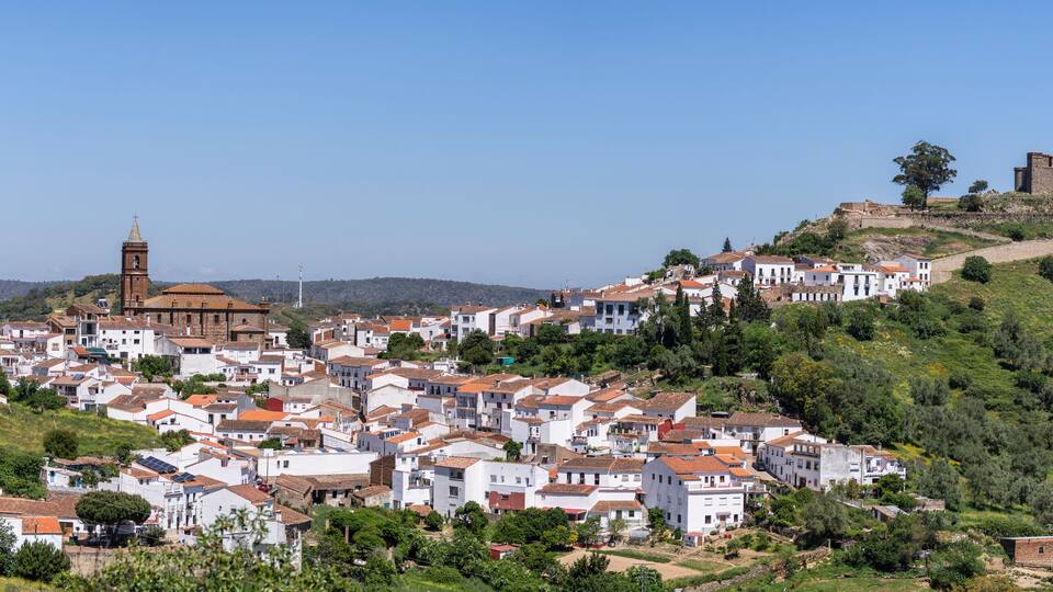 A hillside town with white buildings, a church, and a castle on a hill.