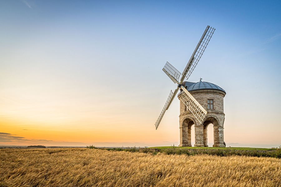 A windmill with a dome roof and lattice structure, set in a field with golden crops under a clear sky.
