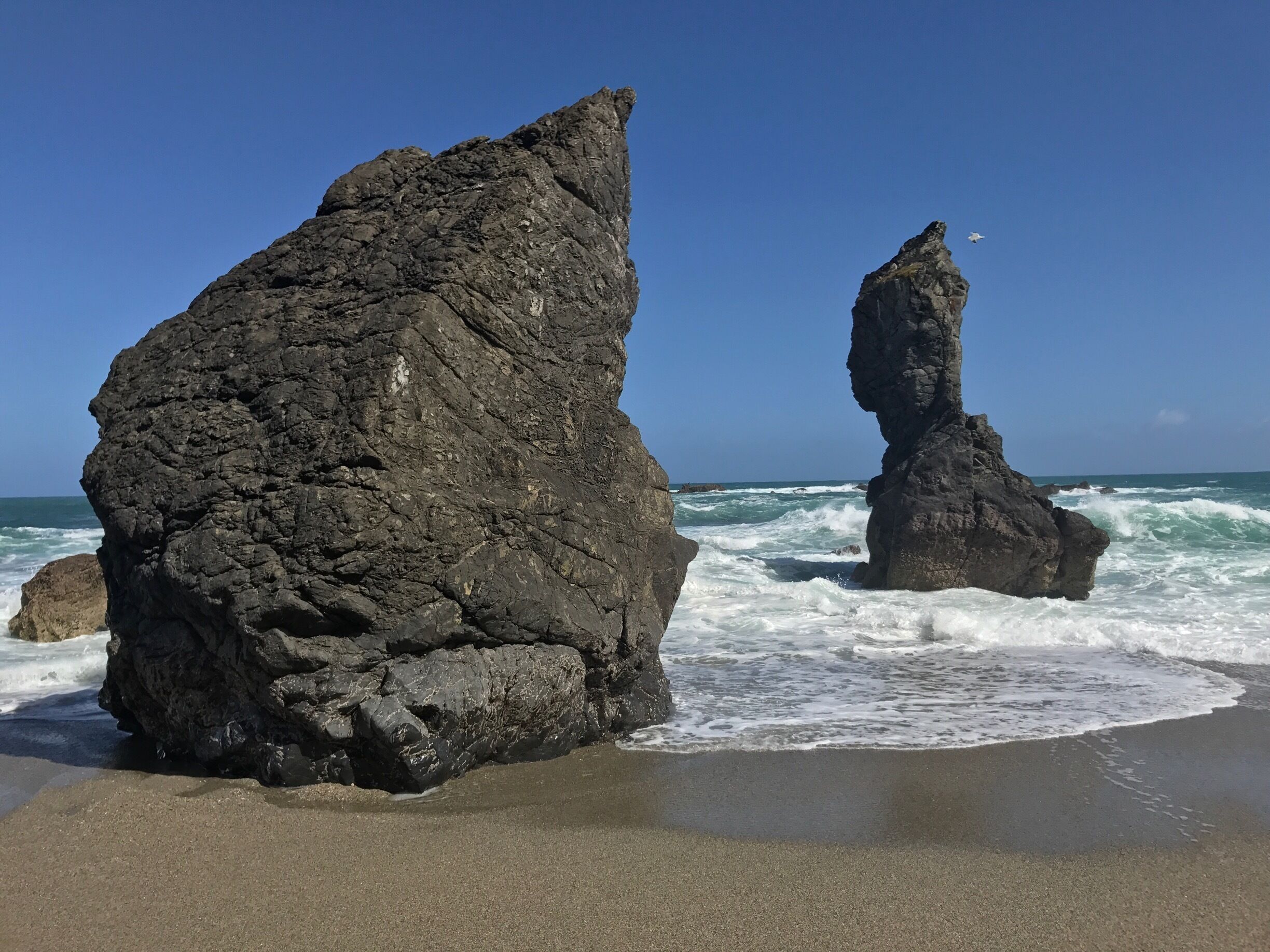 Two prominent rock formations on a beach with waves crashing against them.