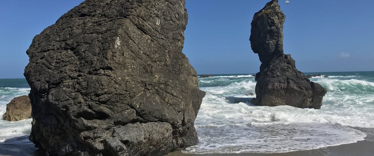 Two prominent rock formations on a beach with waves crashing against them.