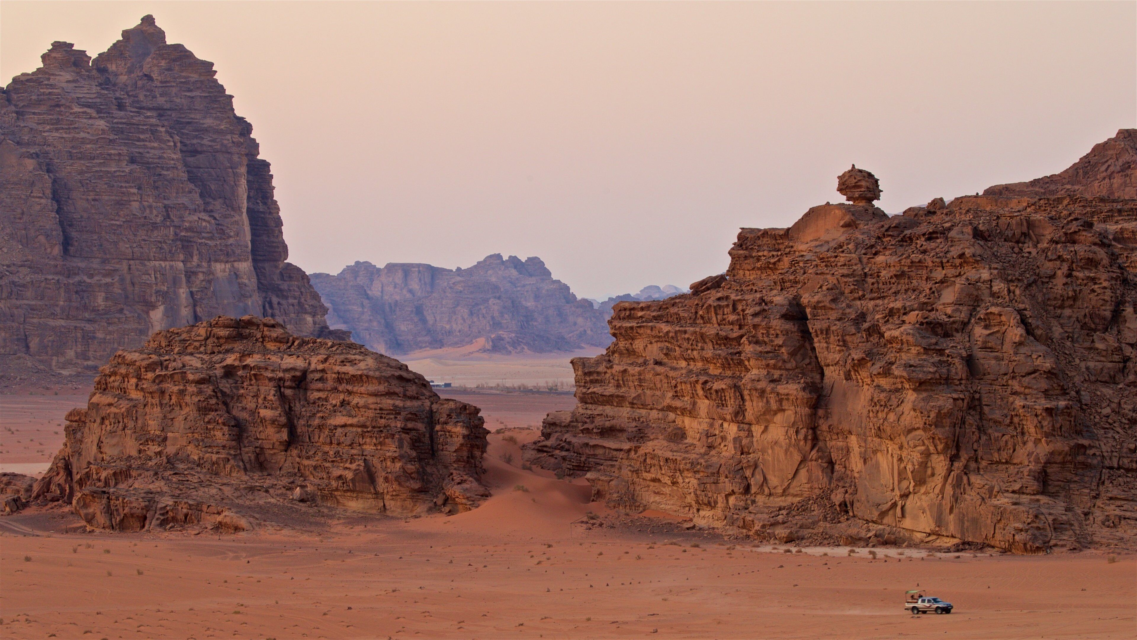 A desert landscape with prominent rock formations and a vehicle in the foreground.