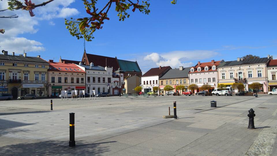 A wide open square with historic buildings, a clear blue sky, and a few cars parked along the street.