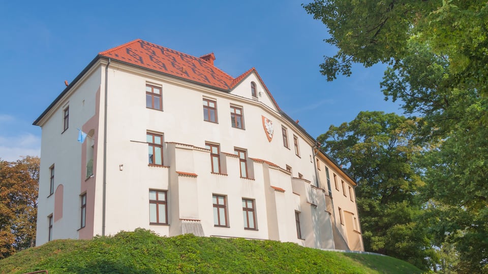 A large white building with a red roof, surrounded by lush greenery and trees.
