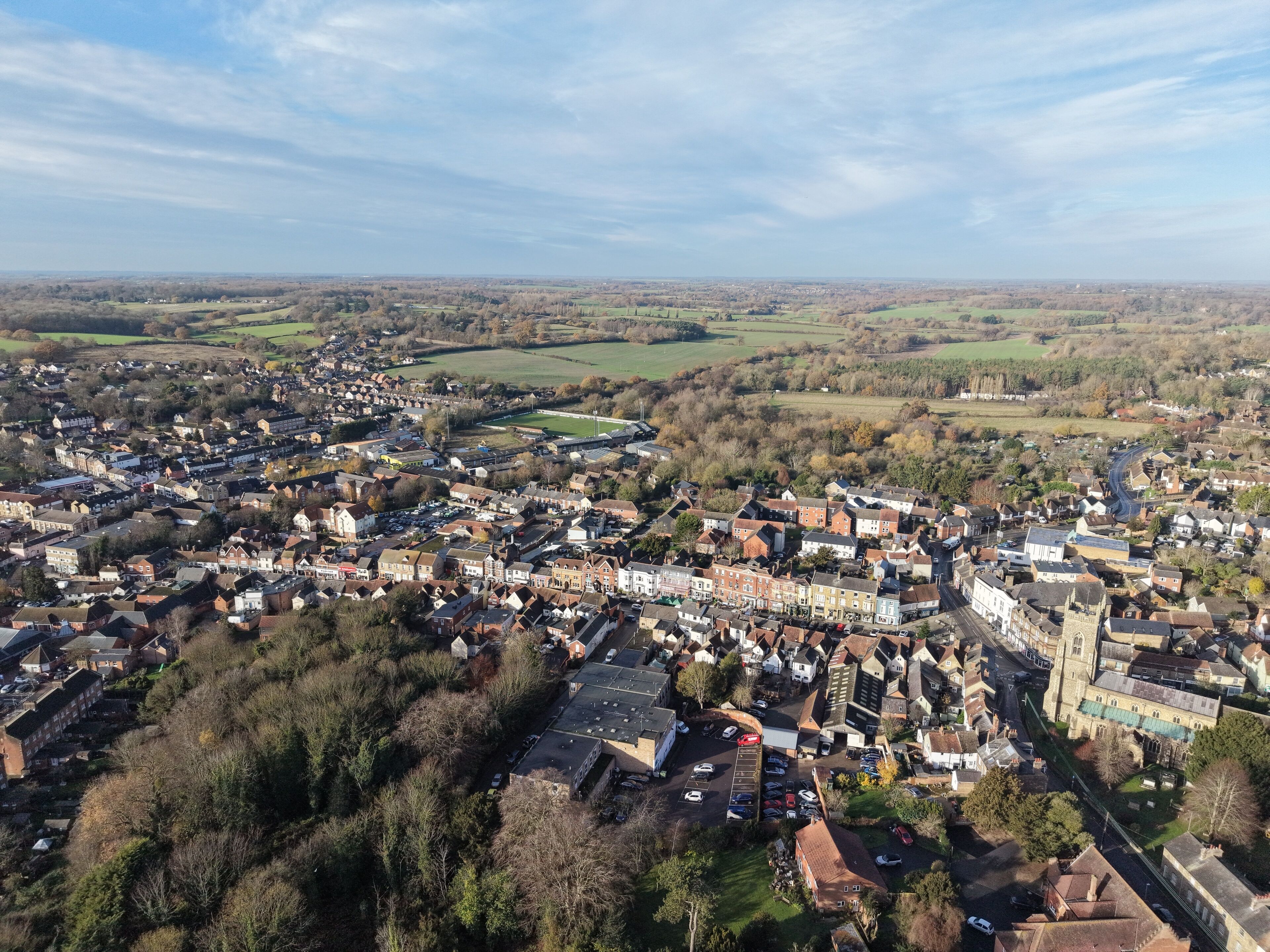 An aerial view of a town with a mix of residential and commercial buildings, surrounded by green fields and open spaces.