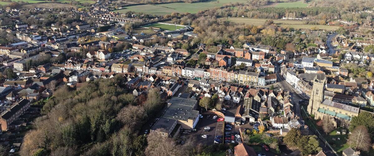An aerial view of a town with a mix of residential and commercial buildings, surrounded by green fields and open spaces.