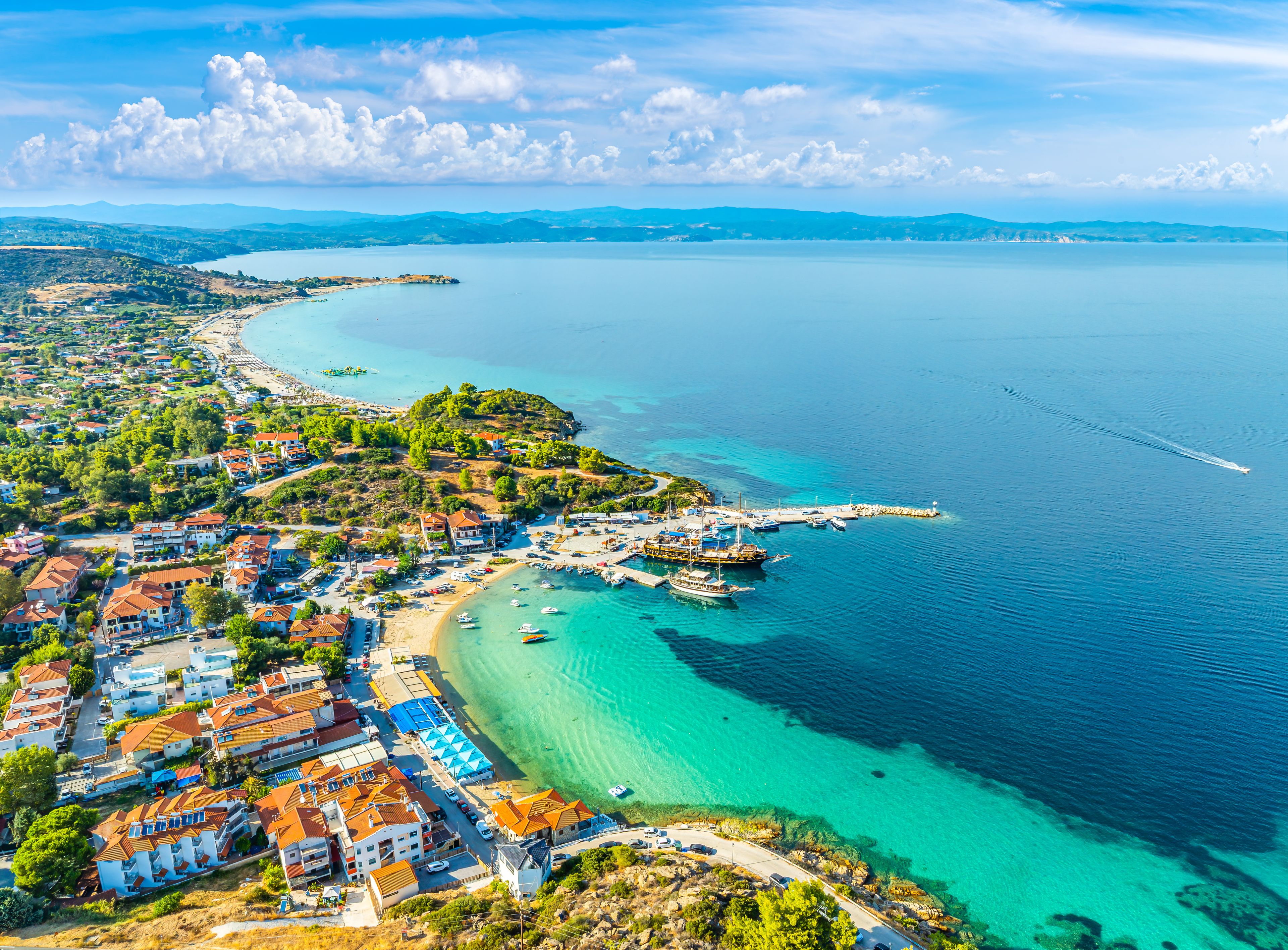 A coastal town with a marina, clear turquoise waters, and a hilly landscape.