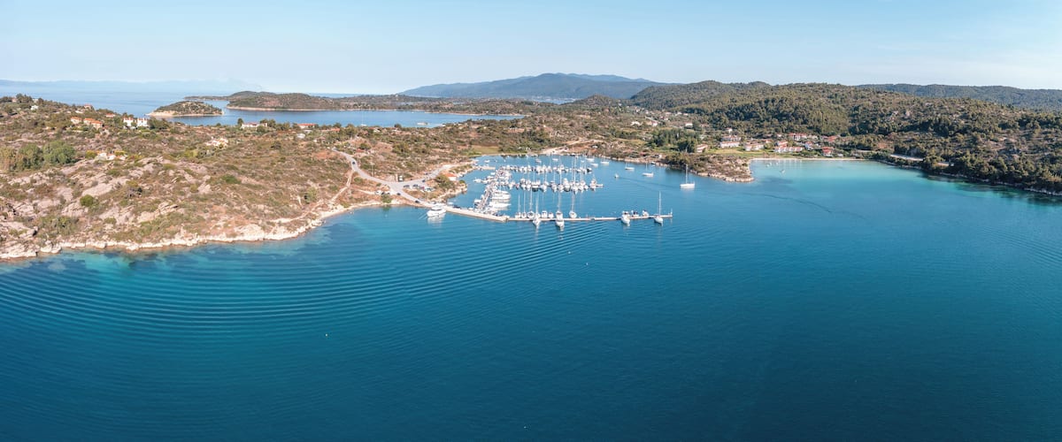 Vue aérienne d’une zone côtière avec un port de plaisance, des bateaux et des collines environnantes.