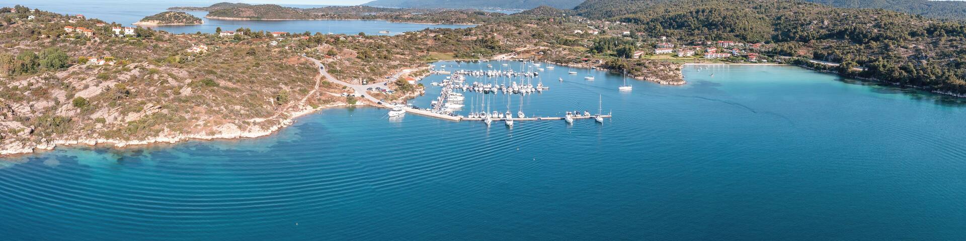 An aerial view of a coastal area with a marina, boats, and surrounding hills.