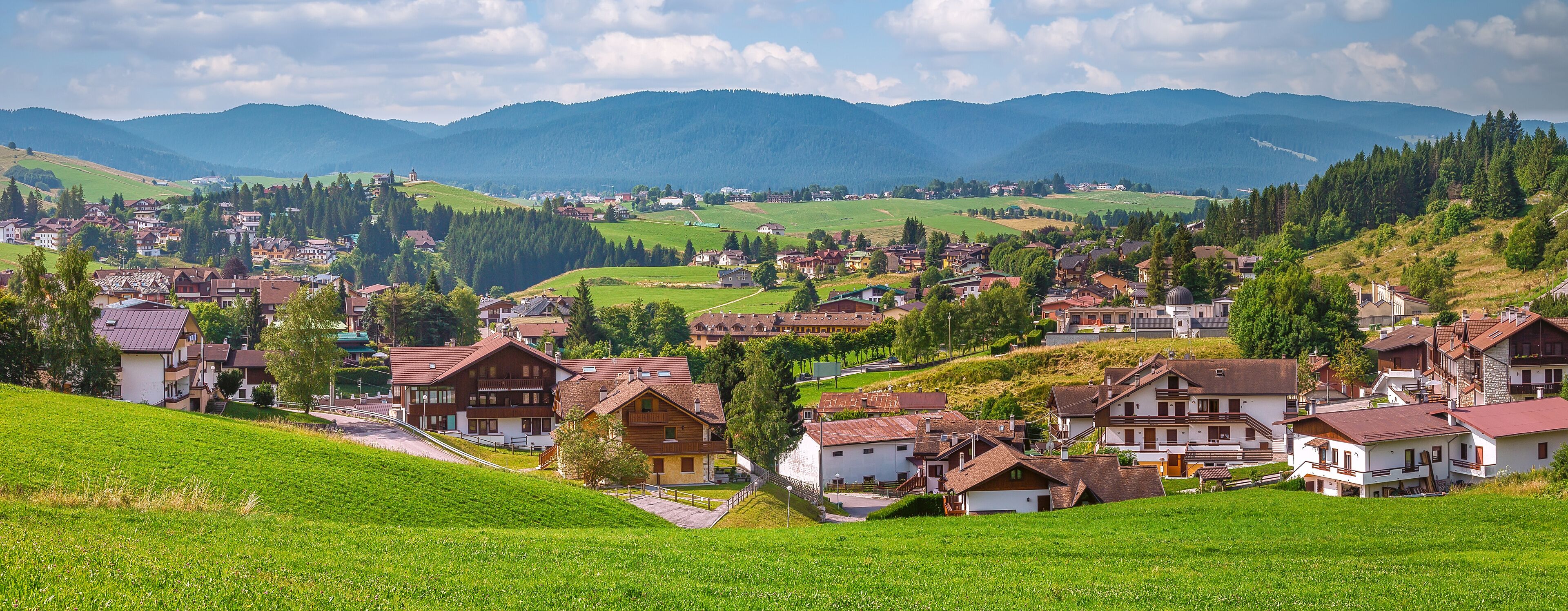 A picturesque village nestled in a valley with rolling hills and mountains in the background.