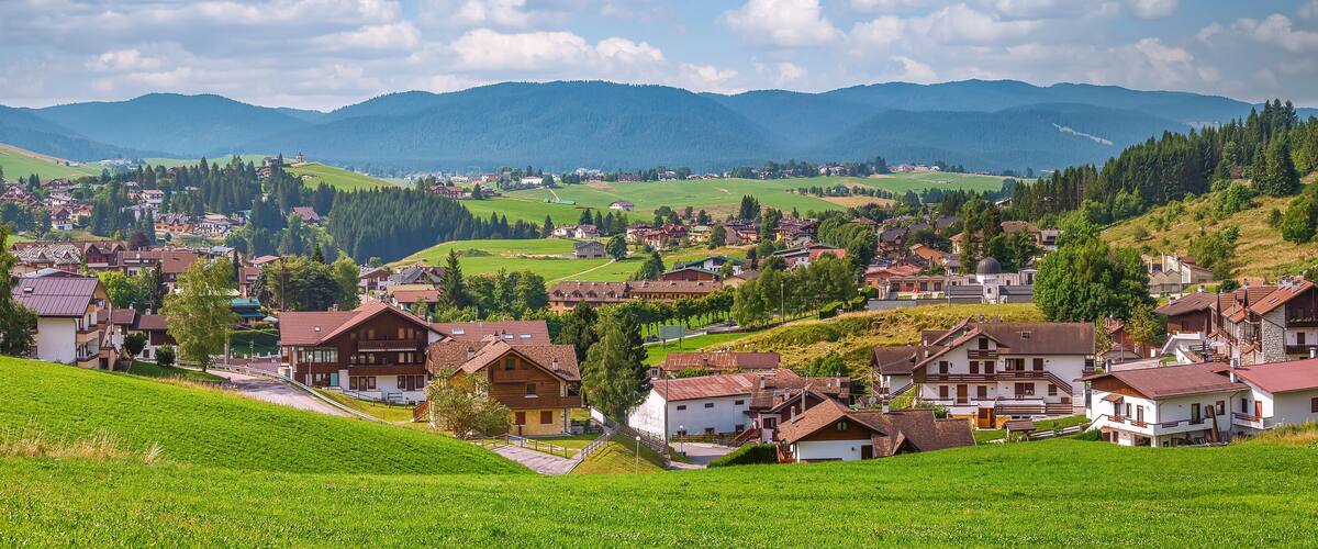 A picturesque village nestled in a valley with rolling hills and mountains in the background.