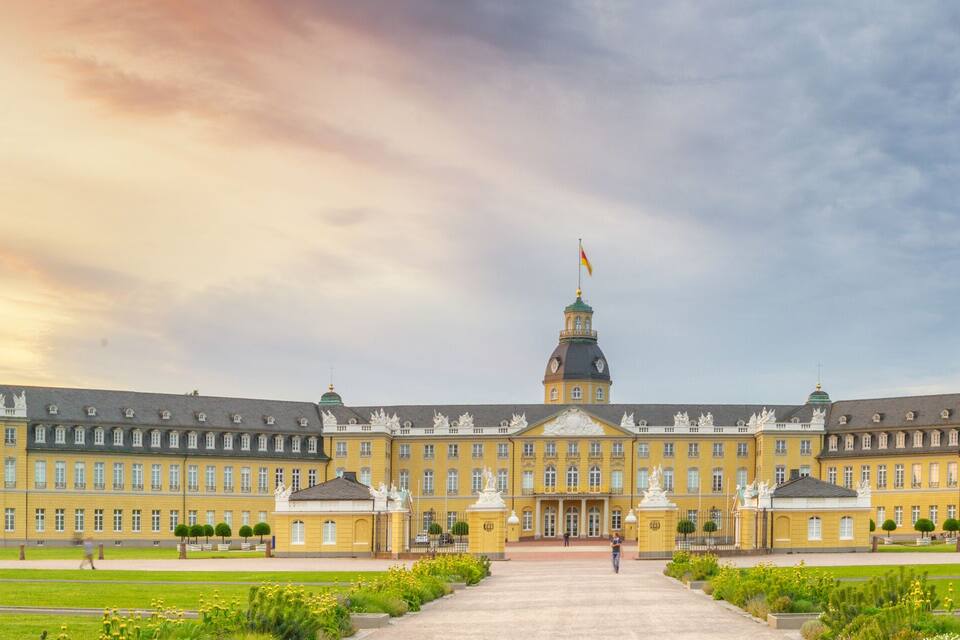 A large yellow building with a central tower, surrounded by a well-manicured lawn and statues.