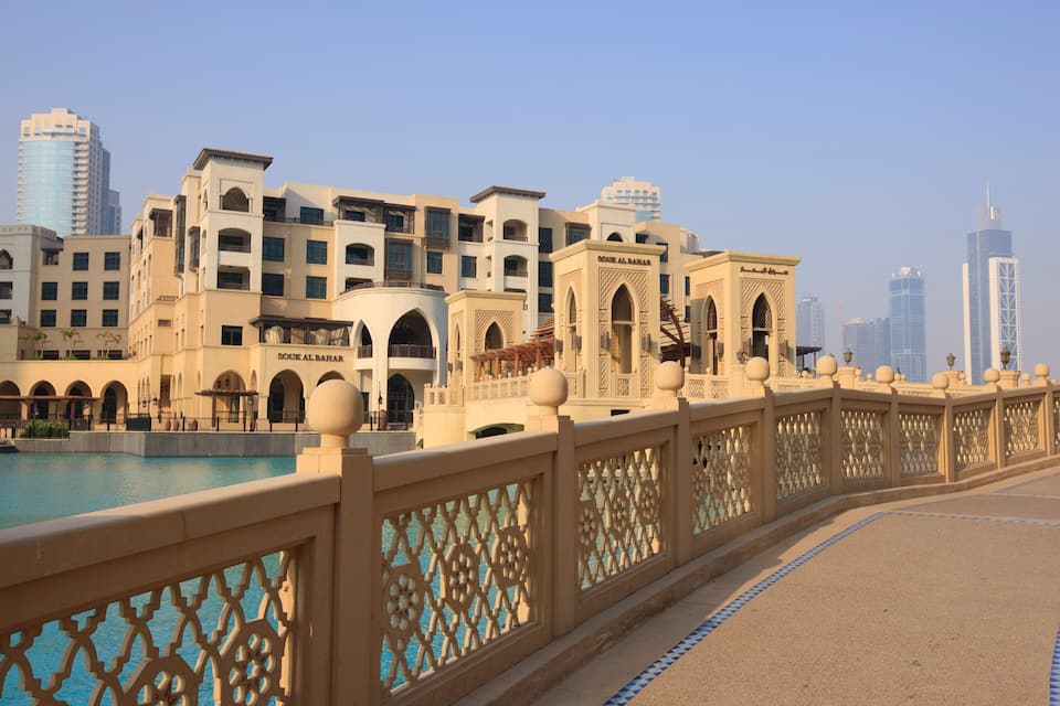 A waterfront promenade with ornate fencing, a pool, and modern buildings including 'SOUK AL BAHAR' and 'SOUK AL BAHAR 2'.