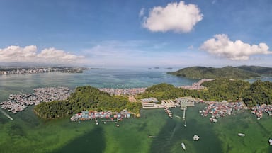 Vista aérea de un pueblo costero con un puerto deportivo, colinas verdes y cielo despejado.