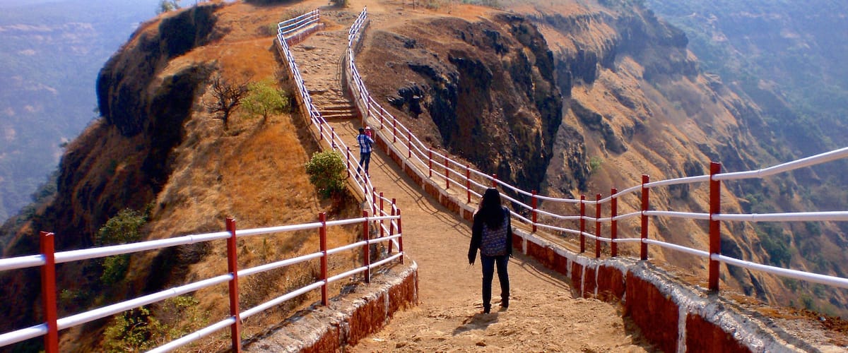 A dirt path with a metal railing leading up a steep hill.