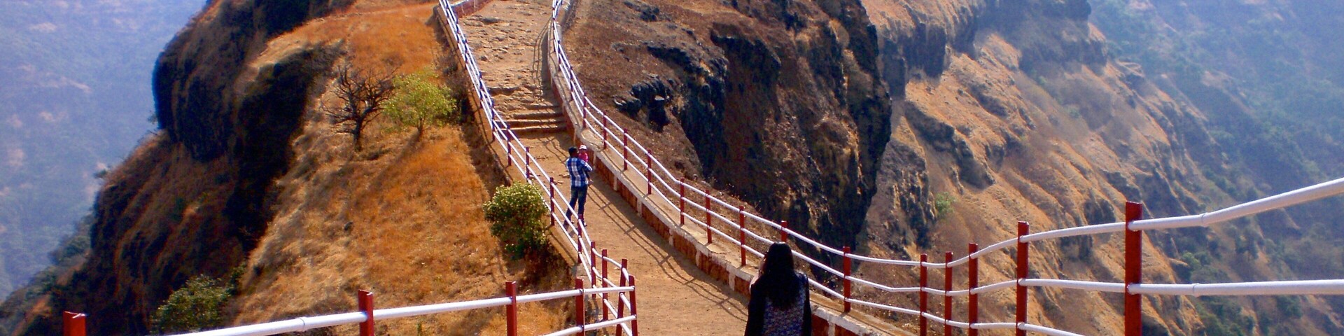 A dirt path with a metal railing leading up a steep hill.
