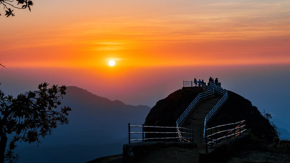 A sunset over a mountainous landscape with a viewing platform and a staircase leading up to it.