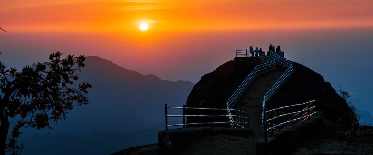 Atardecer sobre un paisaje montañoso con una plataforma de observación y una escalera que conduce a ella.