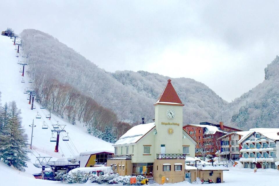 Estación de esquí nevada con una torre del reloj, telesillas y edificios.