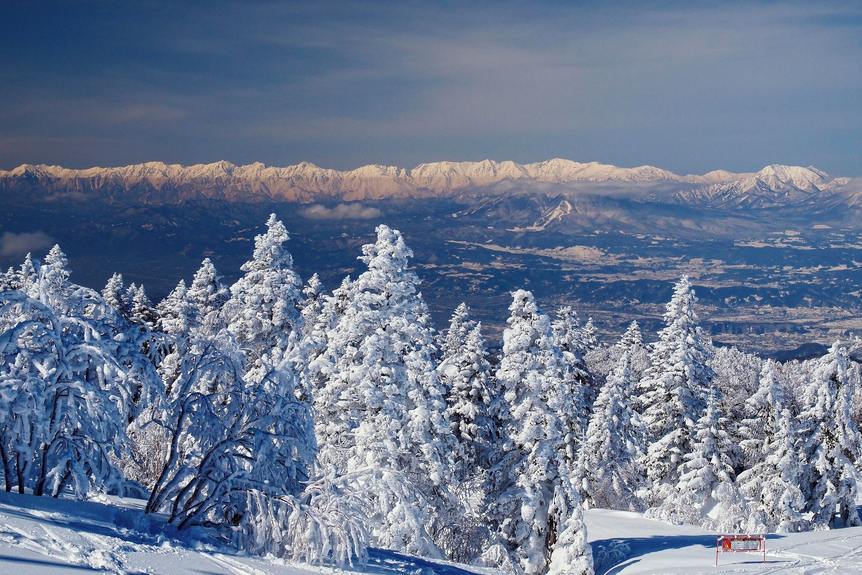 A snow-covered mountain range with a ski resort sign in the foreground.