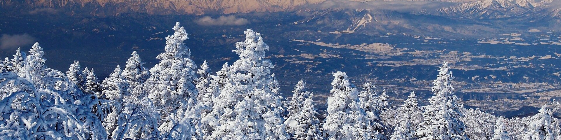 A snow-covered mountain range with a ski resort sign in the foreground.