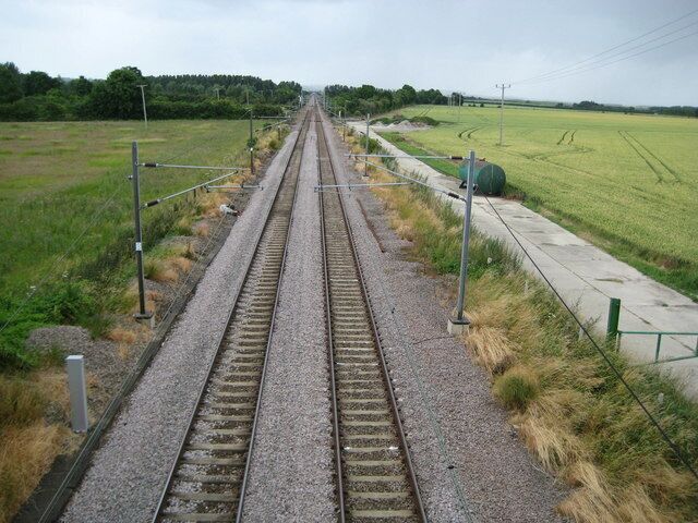 Railway tracks with gravel beds, metal barriers, and a grassy field.