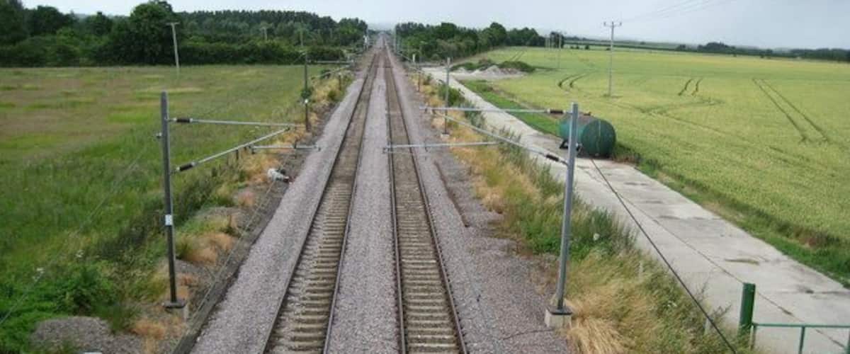 Railway tracks with gravel beds, metal barriers, and a grassy field.