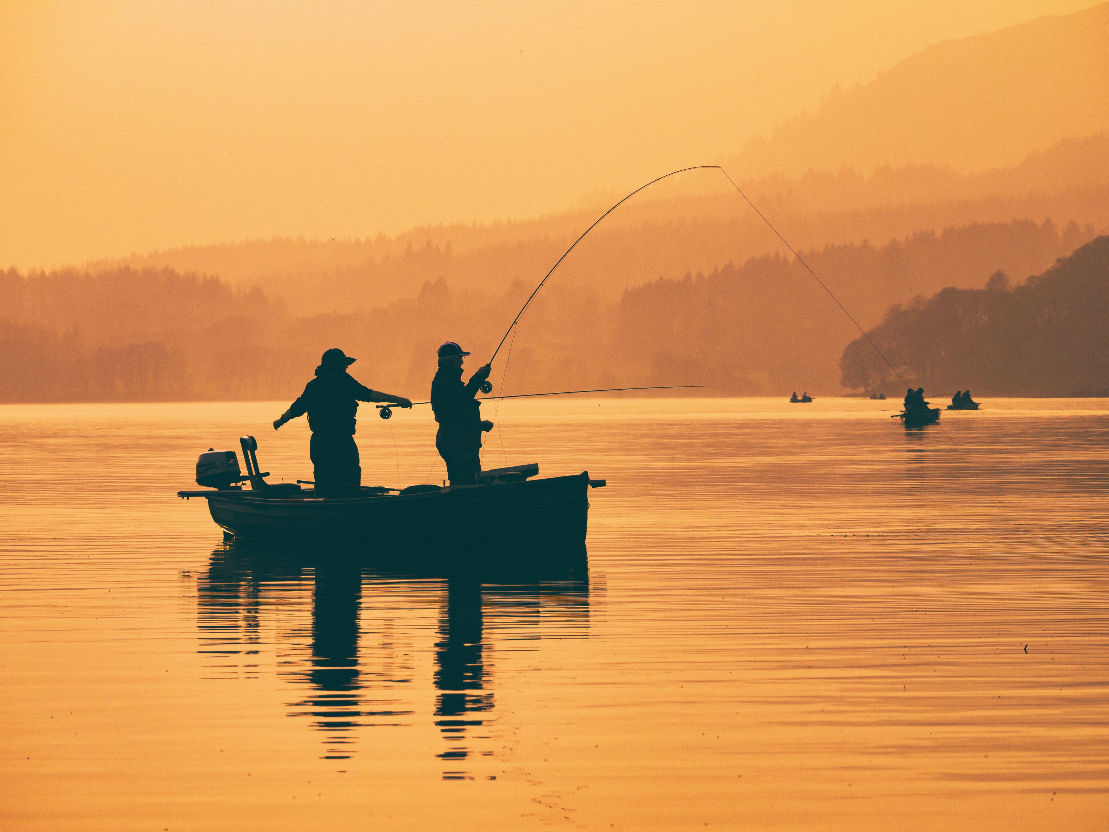 A serene lake with fishing boats and people engaged in fishing, surrounded by a misty forested landscape.