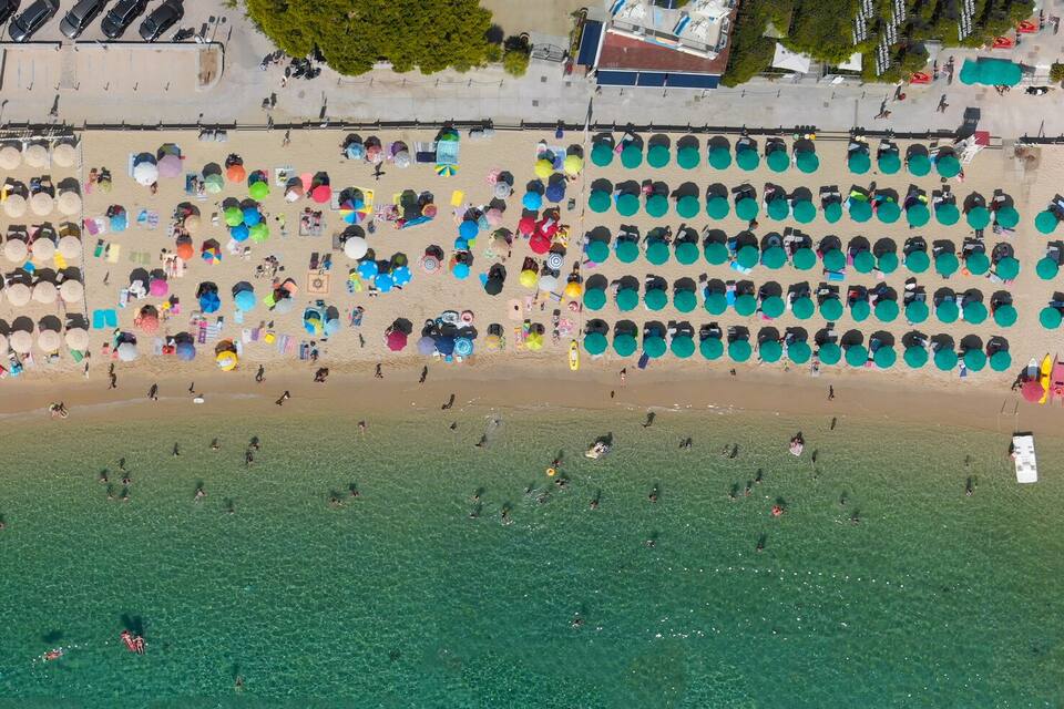 Luftaufnahme eines Strandes mit Reihen von Sonnenschirmen und Menschen.