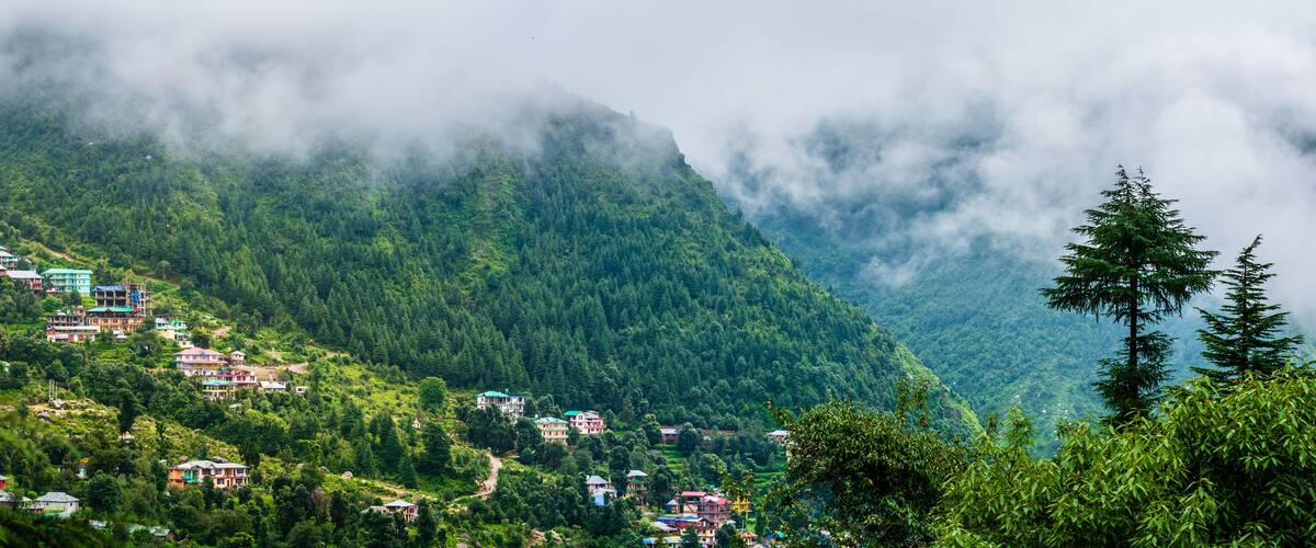 A mountainous village with houses nestled among lush greenery and clouds.
