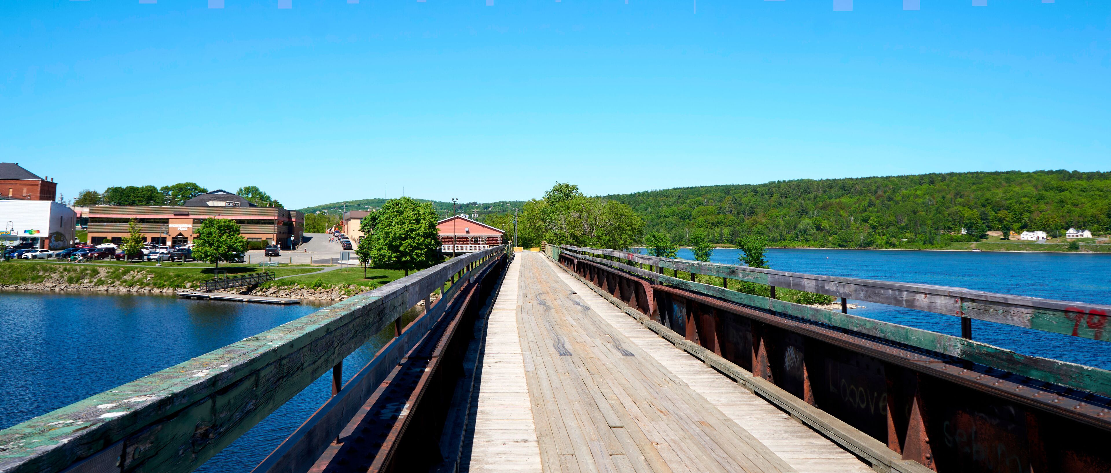 A wooden bridge over a river with a town in the background.