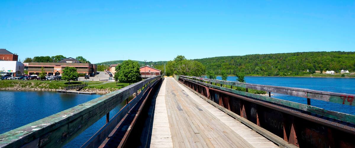 A wooden bridge over a river with a town in the background.