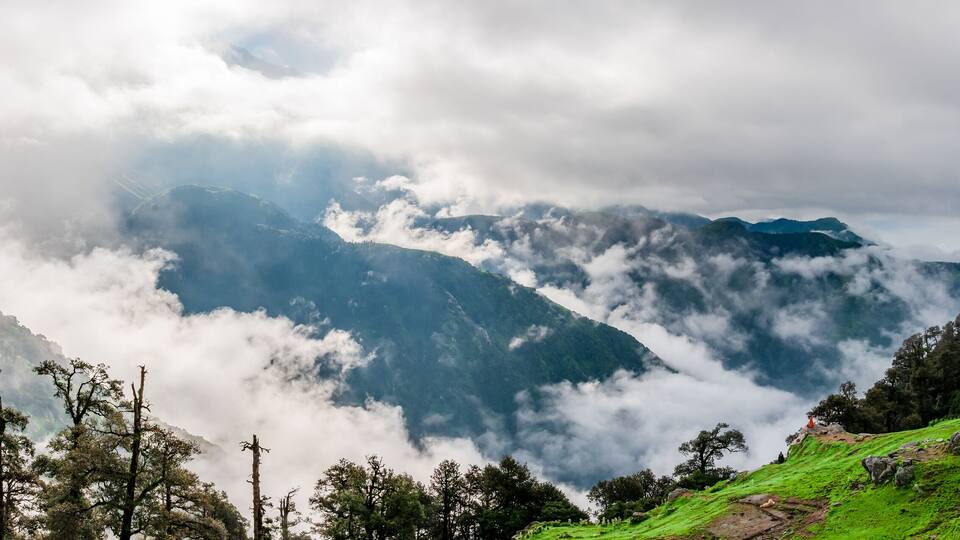 A mountainous landscape with lush green hills, a small building, and a dense cloud cover.