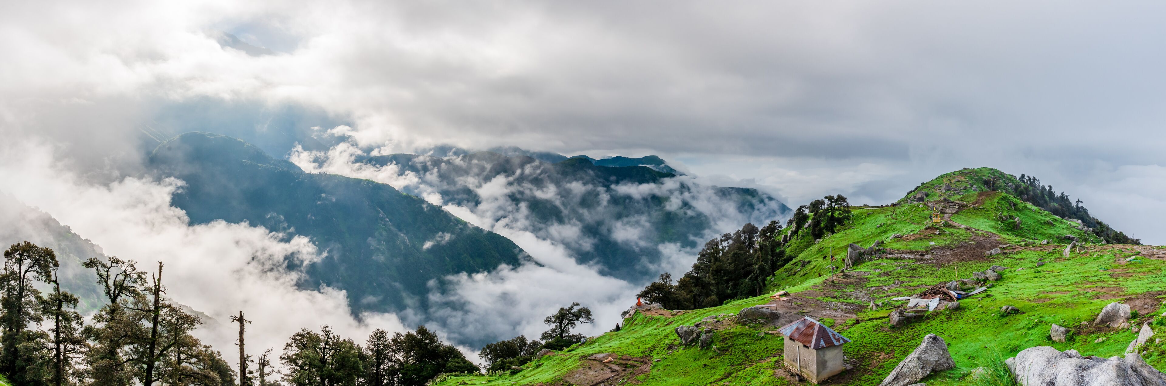 A mountainous landscape with lush green hills, a small building, and a dense cloud cover.