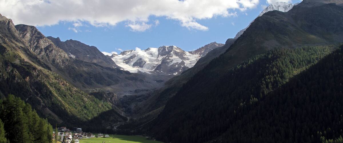 A valley with a mountain range, a small settlement, and a clear sky.