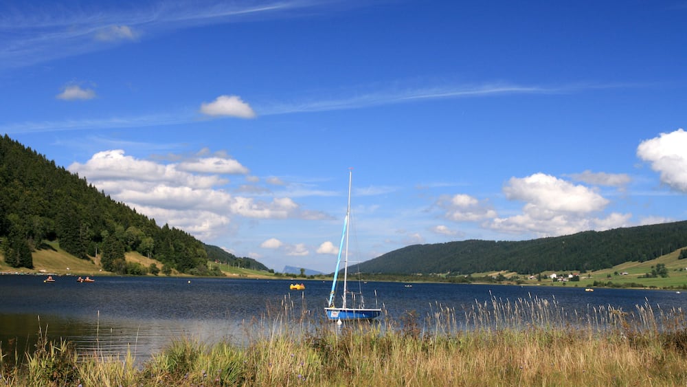 Un voilier sur un lac paisible, entouré de collines et de verdure.