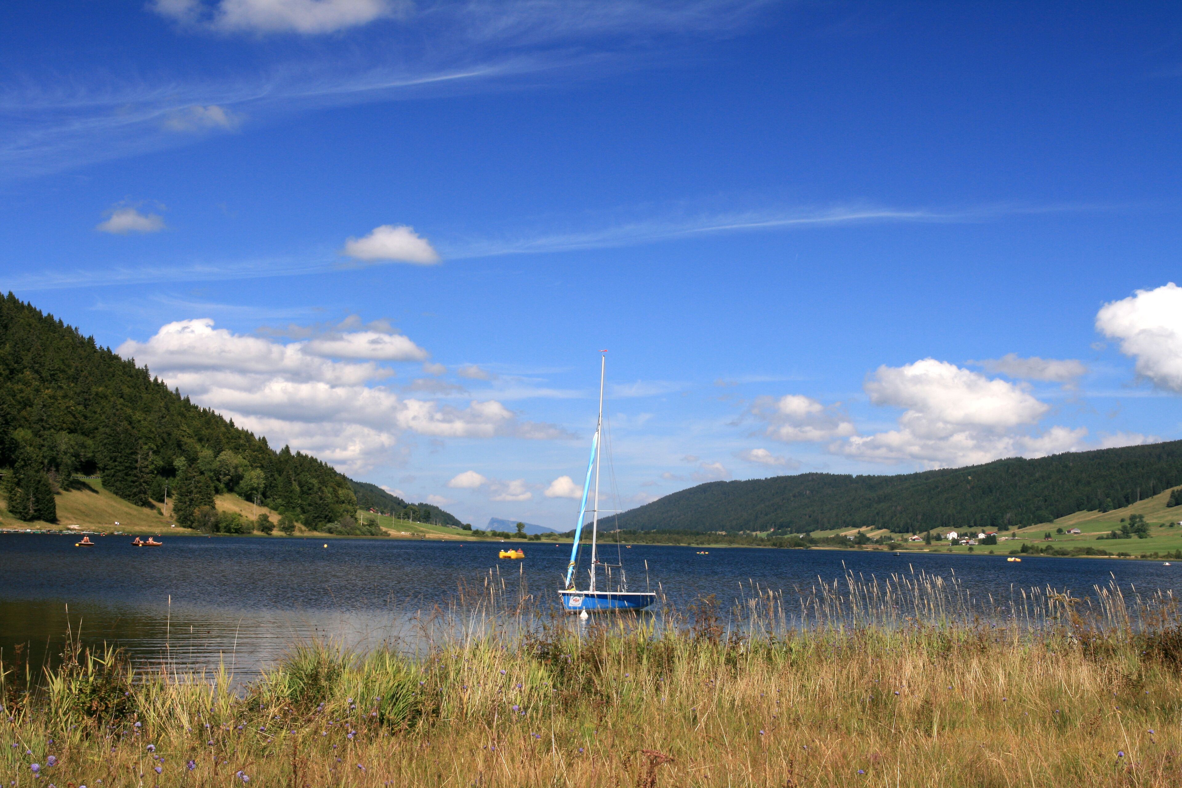 A sailboat on a calm lake surrounded by hills and greenery.