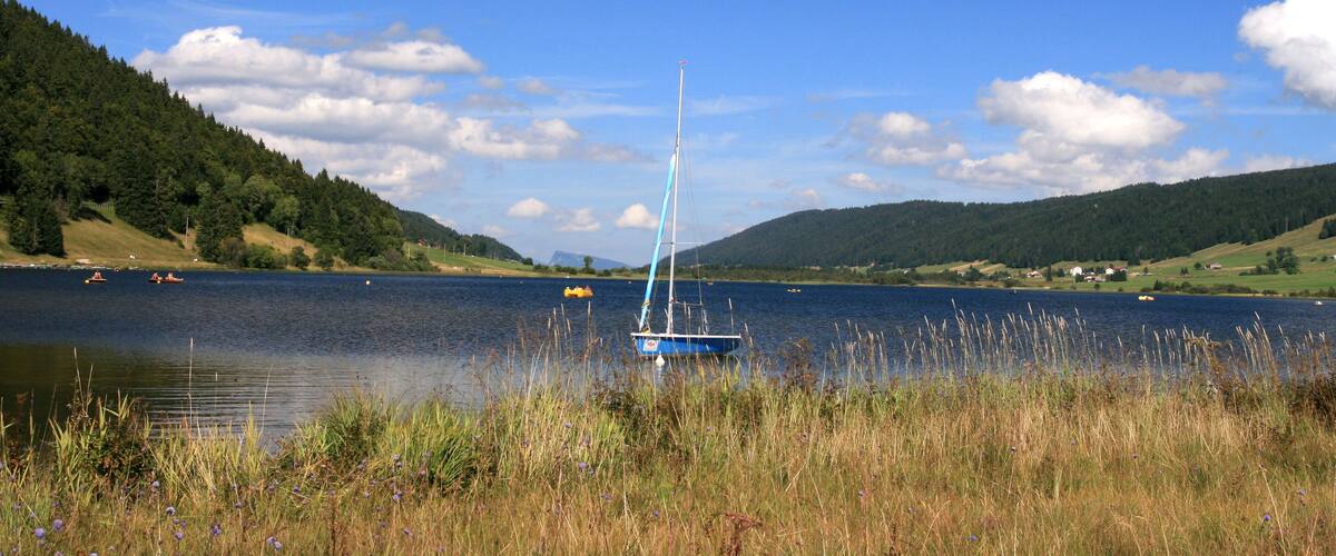 A sailboat on a calm lake surrounded by hills and greenery.