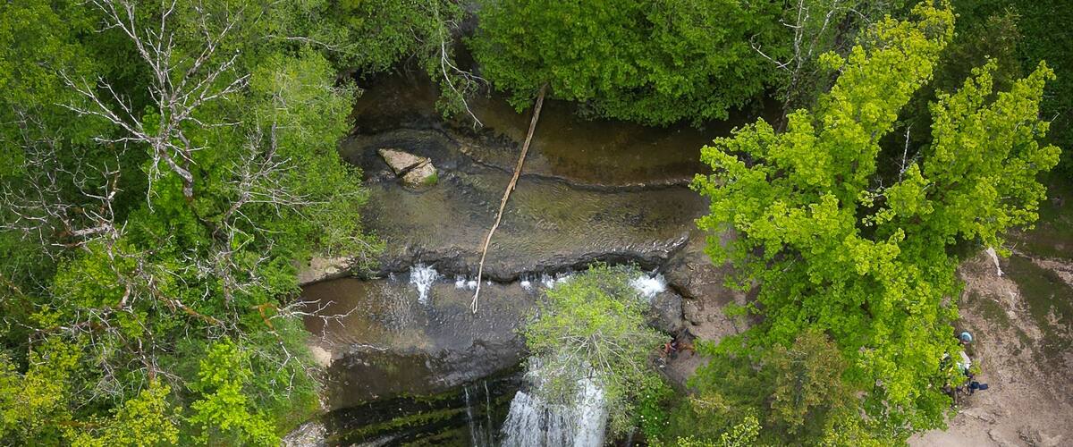 Aerial view of The Herisson waterfalls cascading into a clear pool surrounded by dense green forest and rocky paths in Menetrux-en-Joux, Bourgogne-Franche-Comte, France.