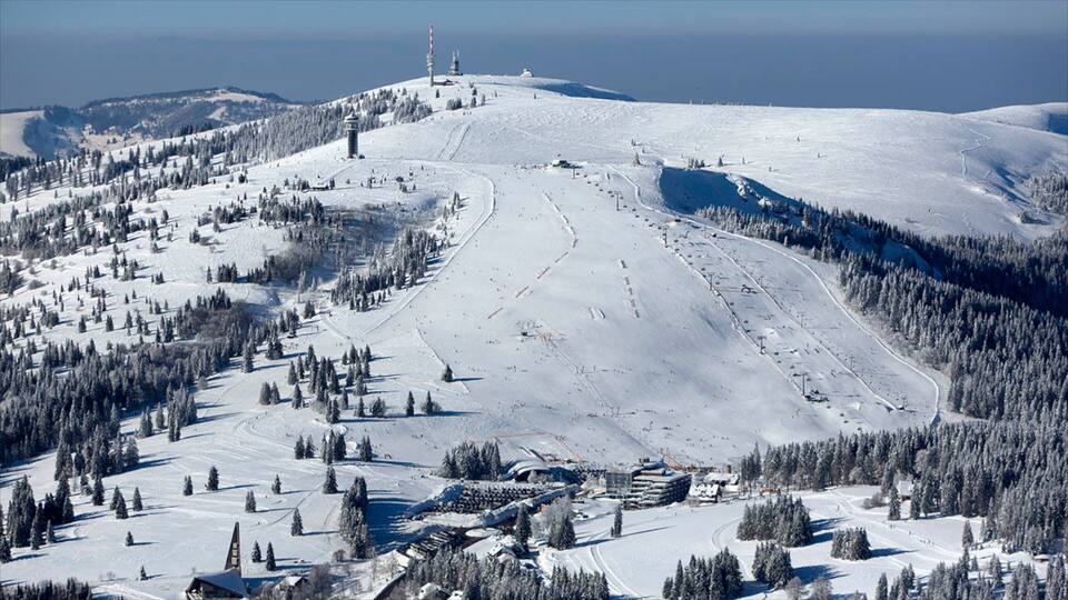 A snow-covered ski slope with ski lifts, trees, and buildings.
