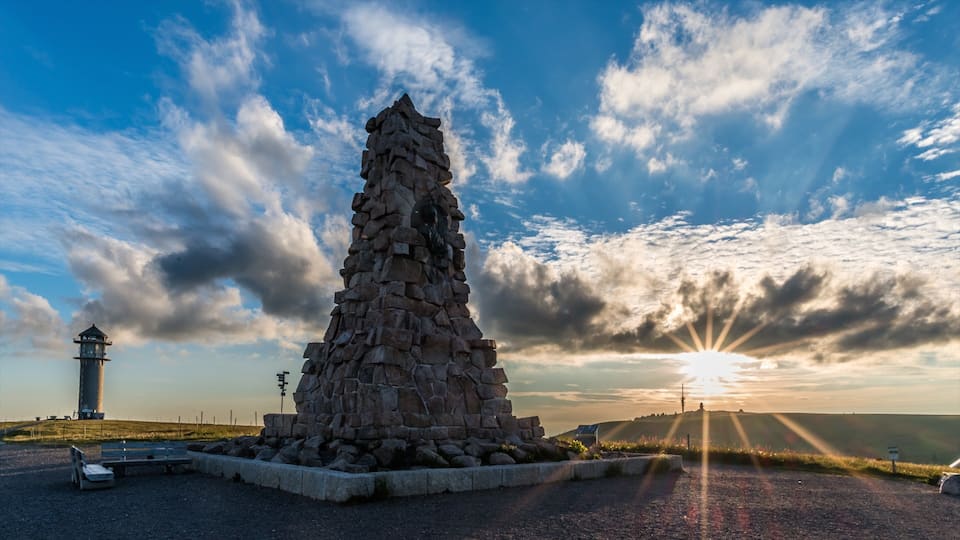 A stone monument, a lighthouse, and a sunset over a hilly landscape.