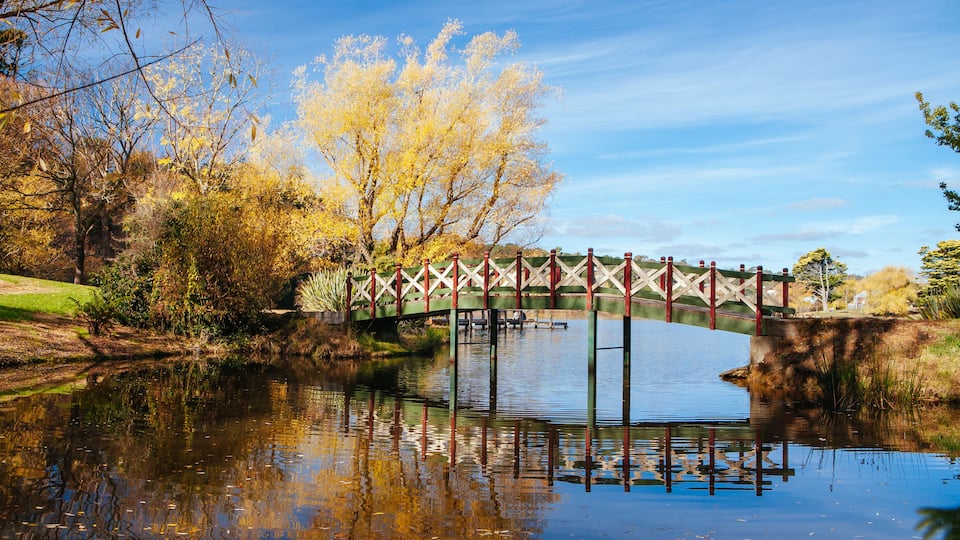 A bridge over a calm river with autumn foliage.